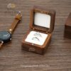 Walnut ring box with a white cushion on a wooden tabletop